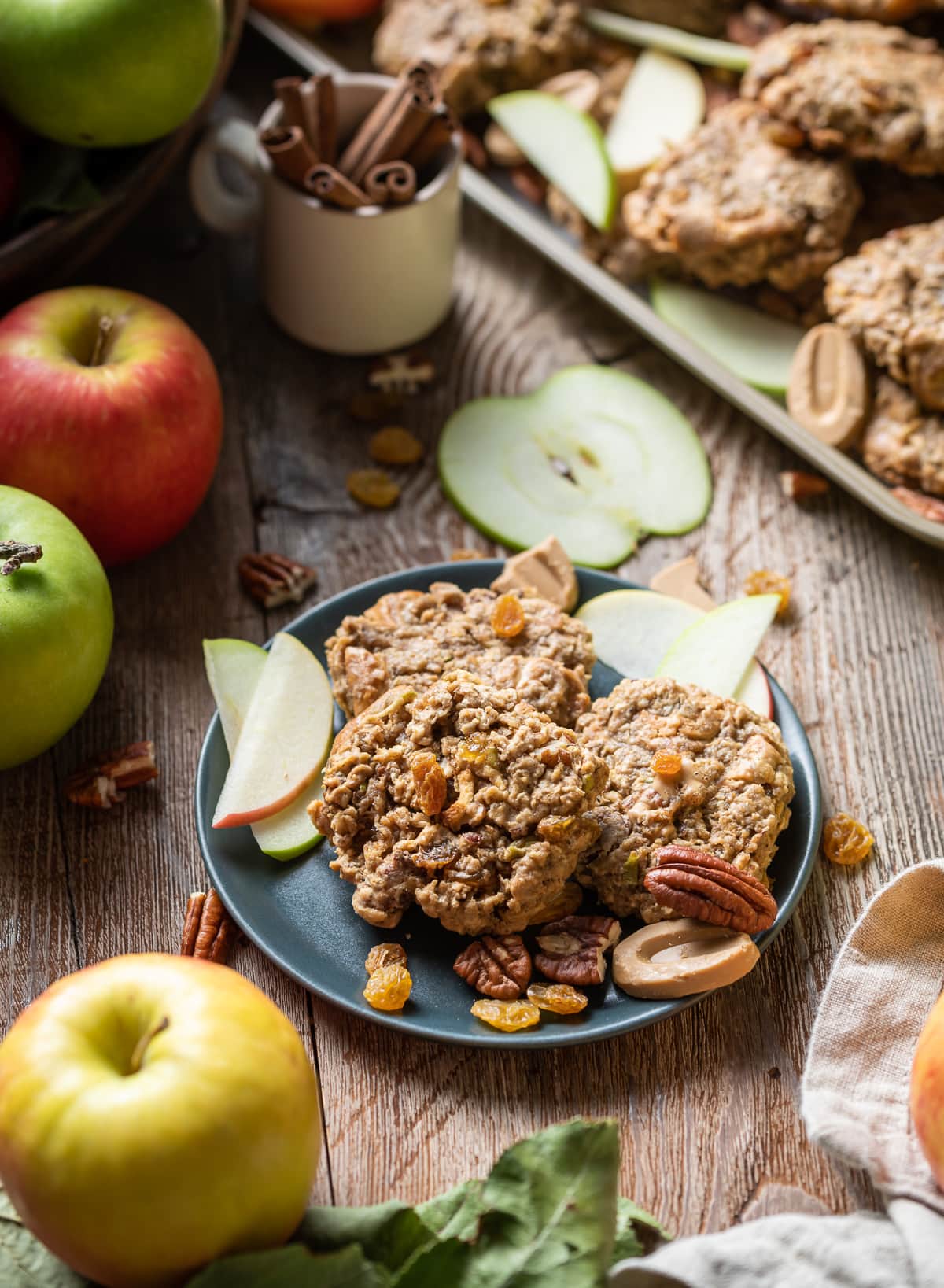 apple oatmeal cookies on a plate with pecans apple slices golden raisins and whole red and green apples