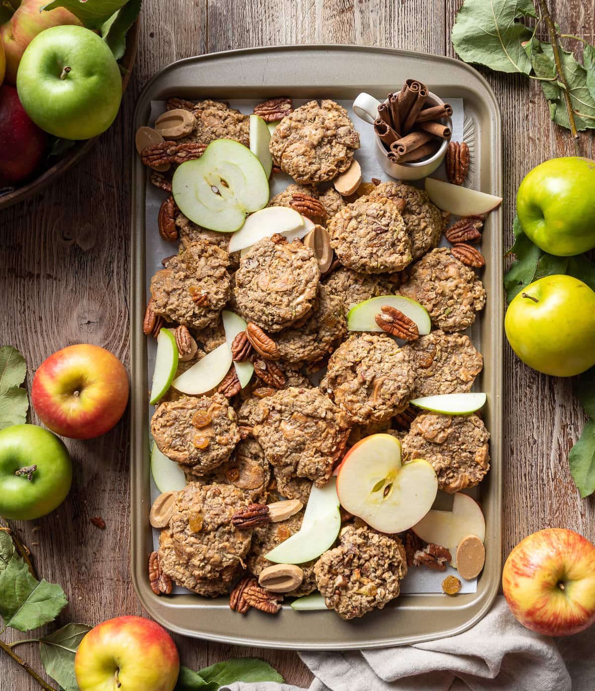 apple oatmeal cookies on a tray with pecans apple slices golden raisins and whole red and green apples