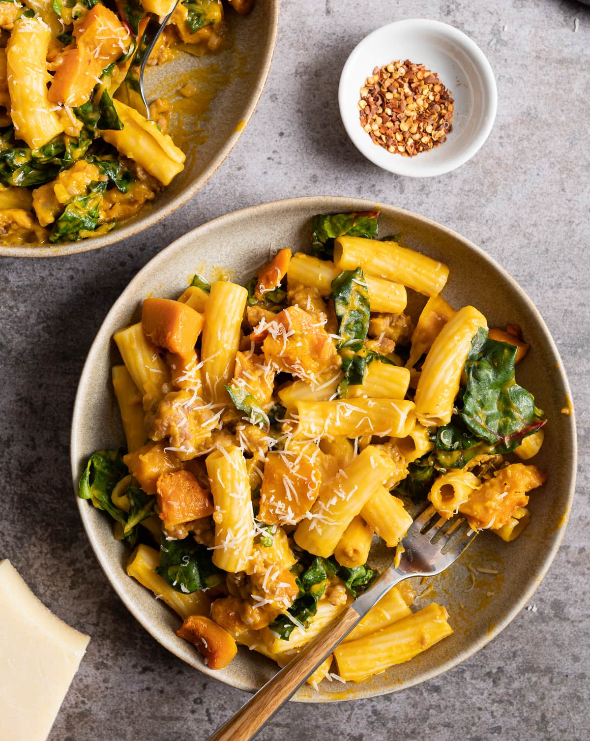 Beige bowl with orange yellow honeynut squash pasta green chard bowl or red pepper flakes fork