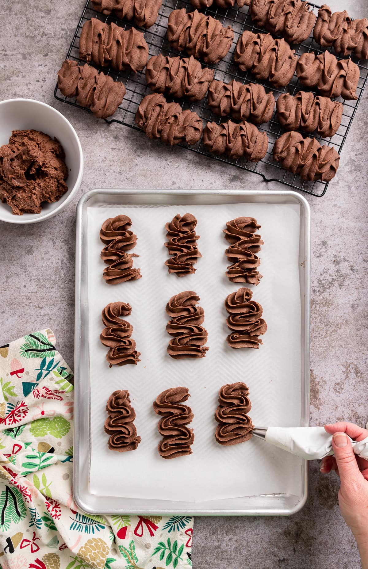 chocolate viennese butter cookies being piped on a tray lined with white parchment paper