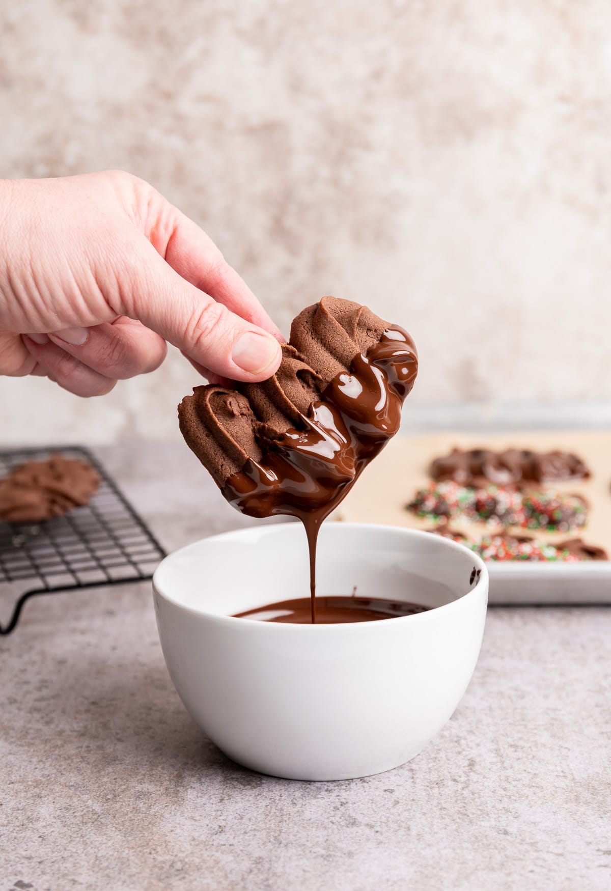 chocolate viennese butter cookie being half dipped in a bowl of melted chocolate