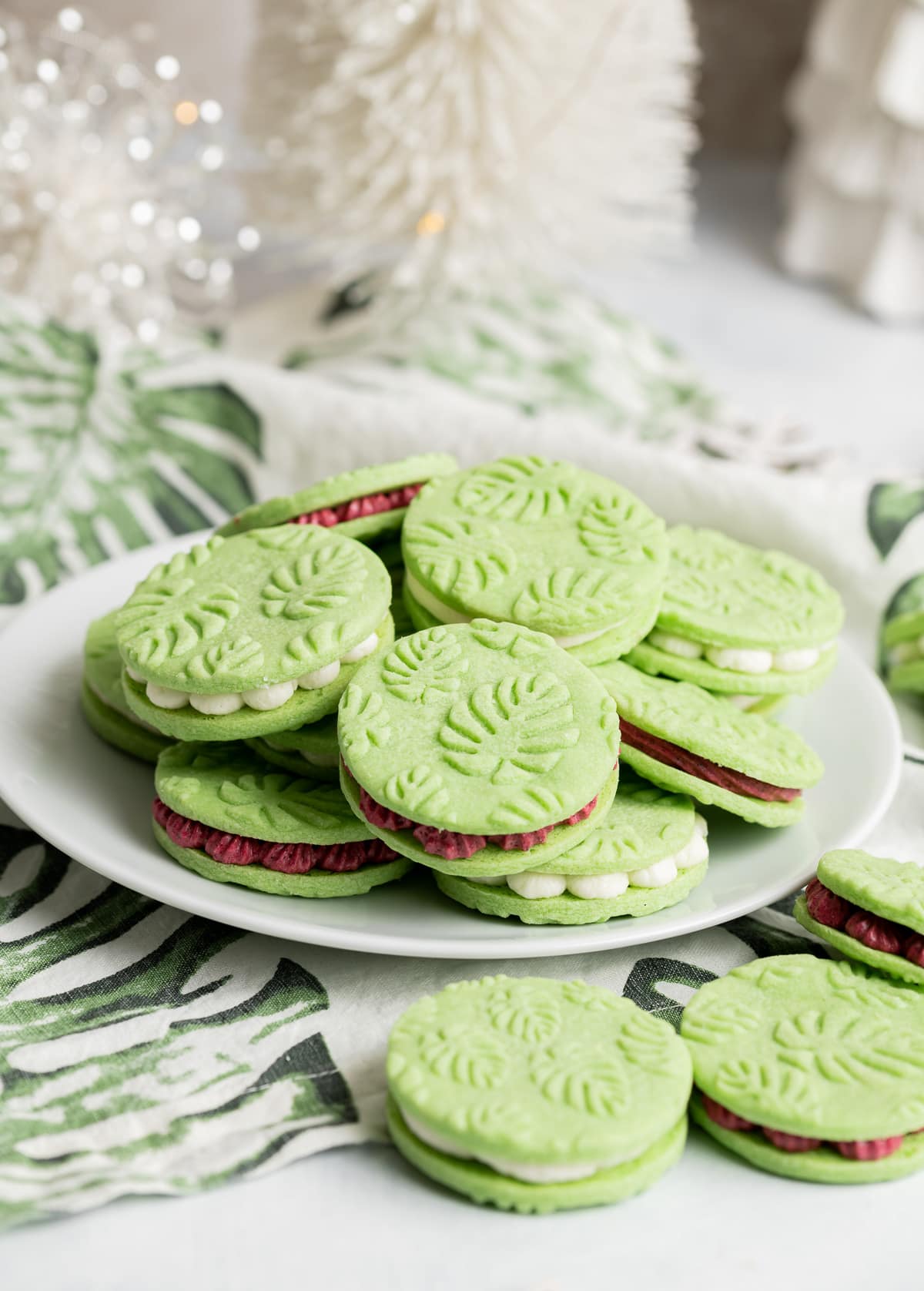 green pandan sandwich cookies with white and red buttercream filling and an embossed monstera leaf pattern on the cookies