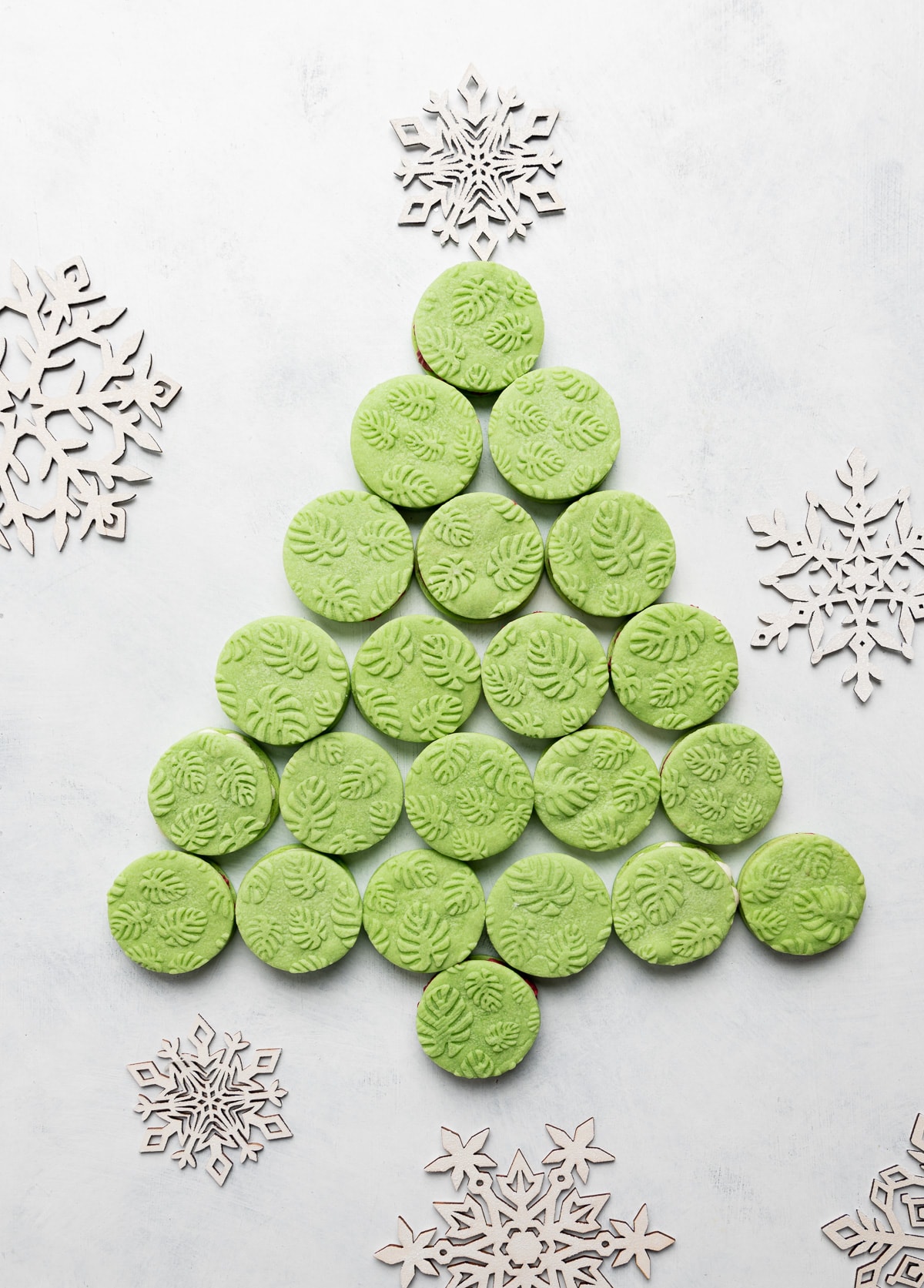 green monstera leaf round cookies arranged to look like a christmas tree with white wooden snowflakes