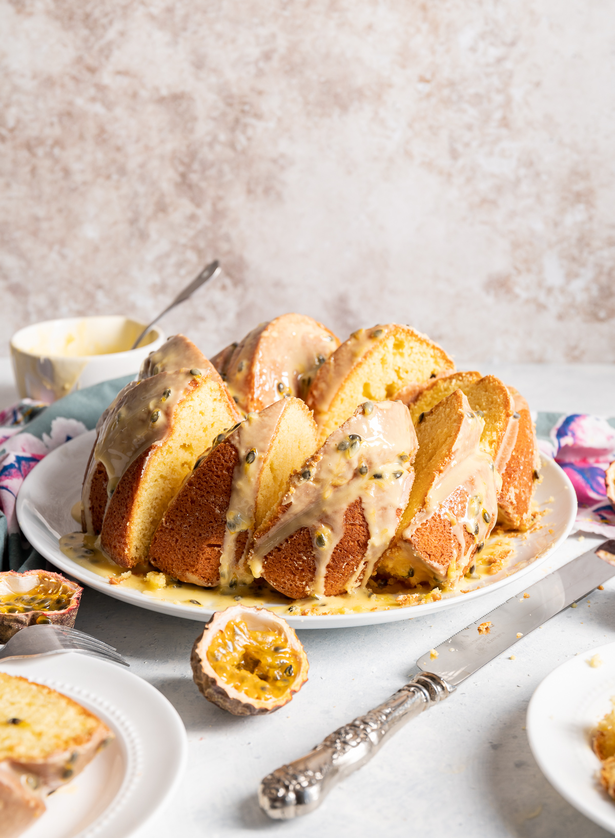 yellow passionfruit bundt cake sliced on a large white plate slices on smaller white plates pink and blue napkins whole and halved passion fruits