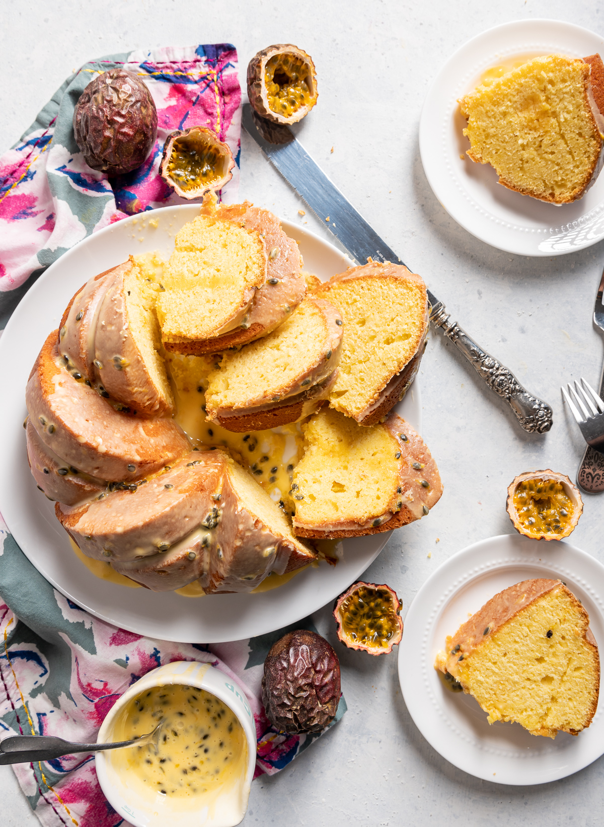 yellow passionfruit bundt cake sliced on a large white plate slices on smaller white plates pink and blue napkins whole and halved passion fruits