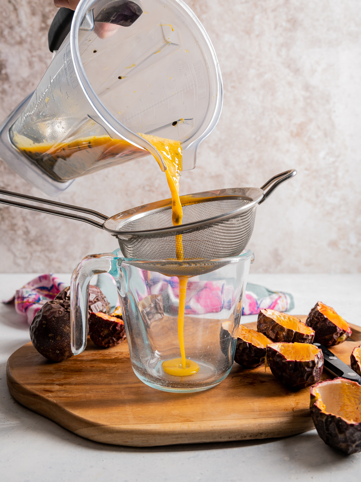 passion fruit juice being strained into a measuring cup from a blender cutting board passion fruits cut in half