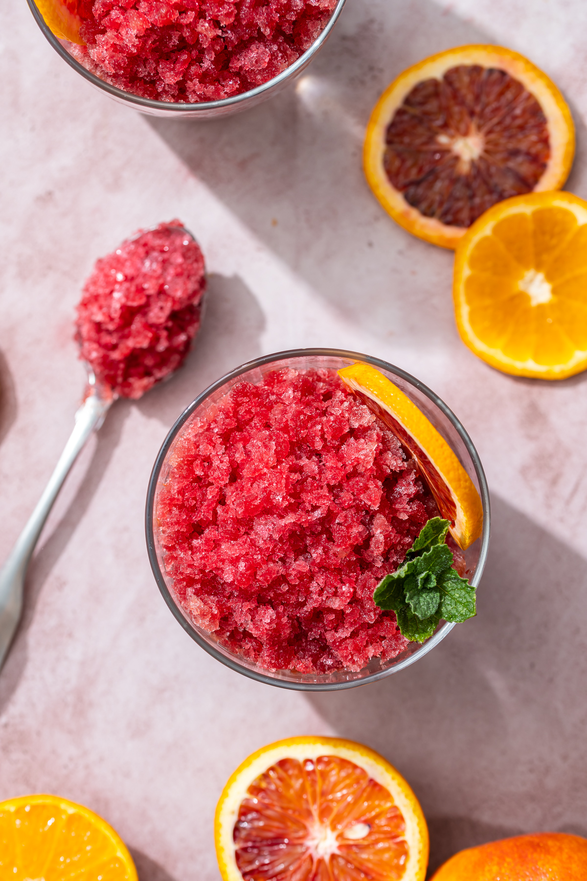 reddish orange blood orange granita in glasses spoons blood orange and tangerine slices