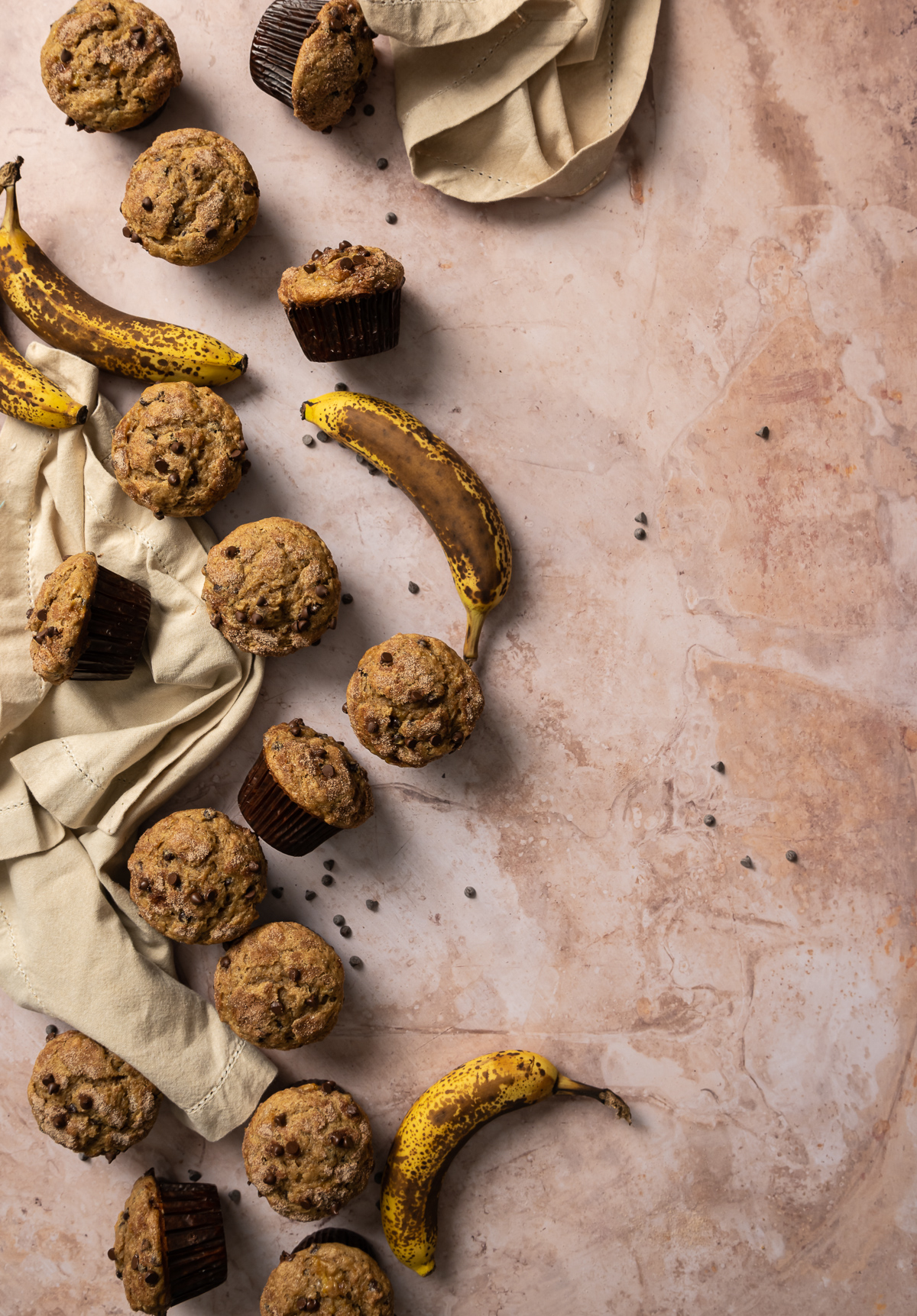 banana muffins in brown wrappers scattered about tan napkin spotty bananas
