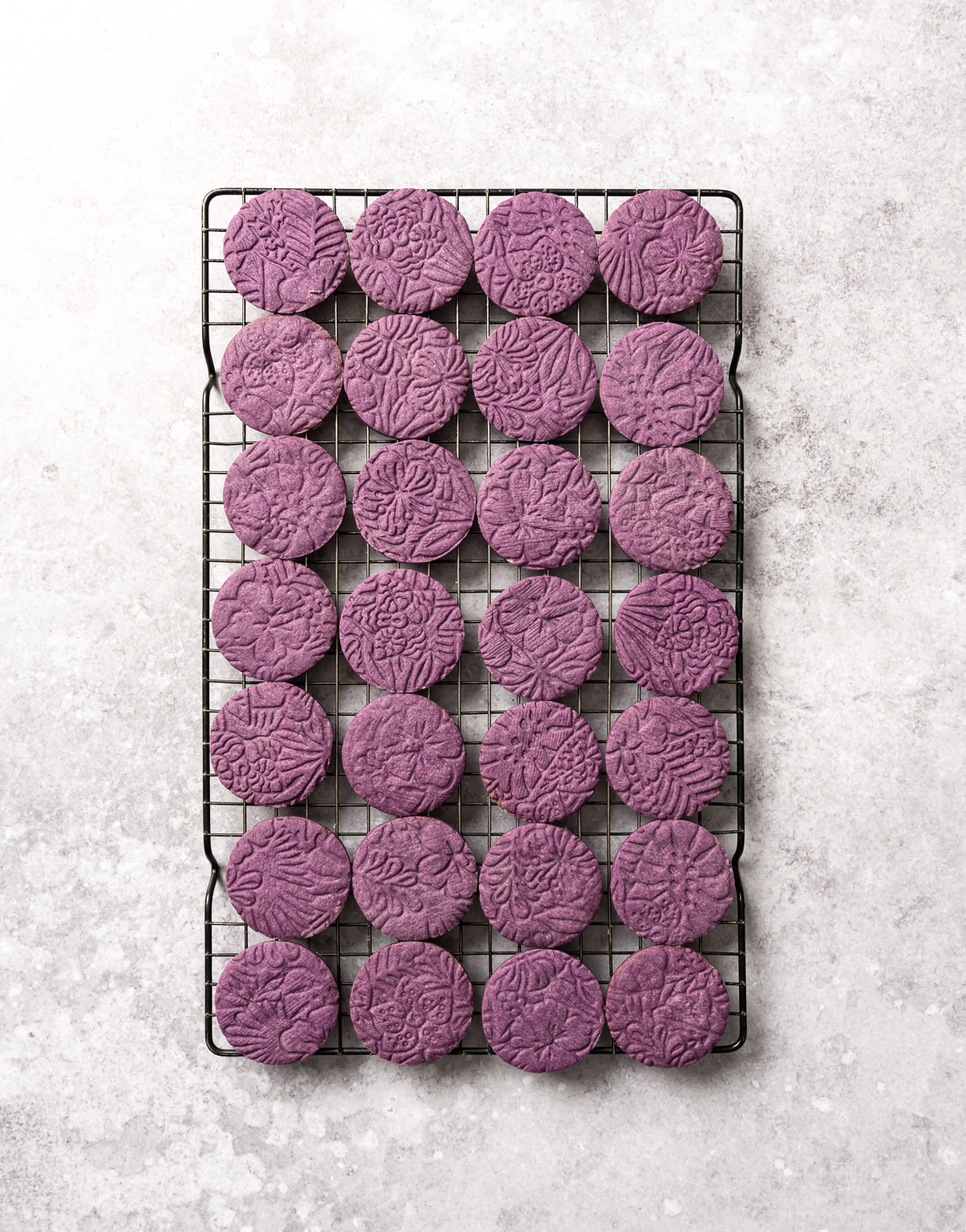 baked round embossed purple cookies on wire cooling rack
