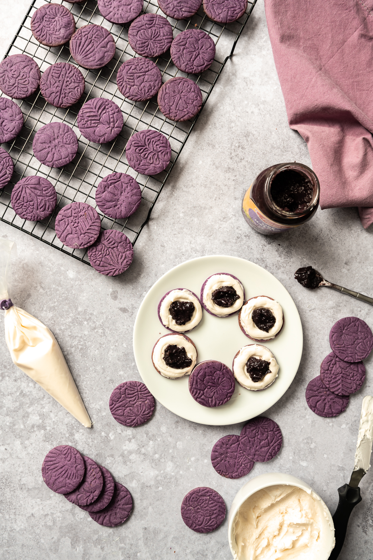 round embossed purple cookies on a wire cooling rack, jar of ube halaya jam cookies on a plate bowl of white coconut frosting