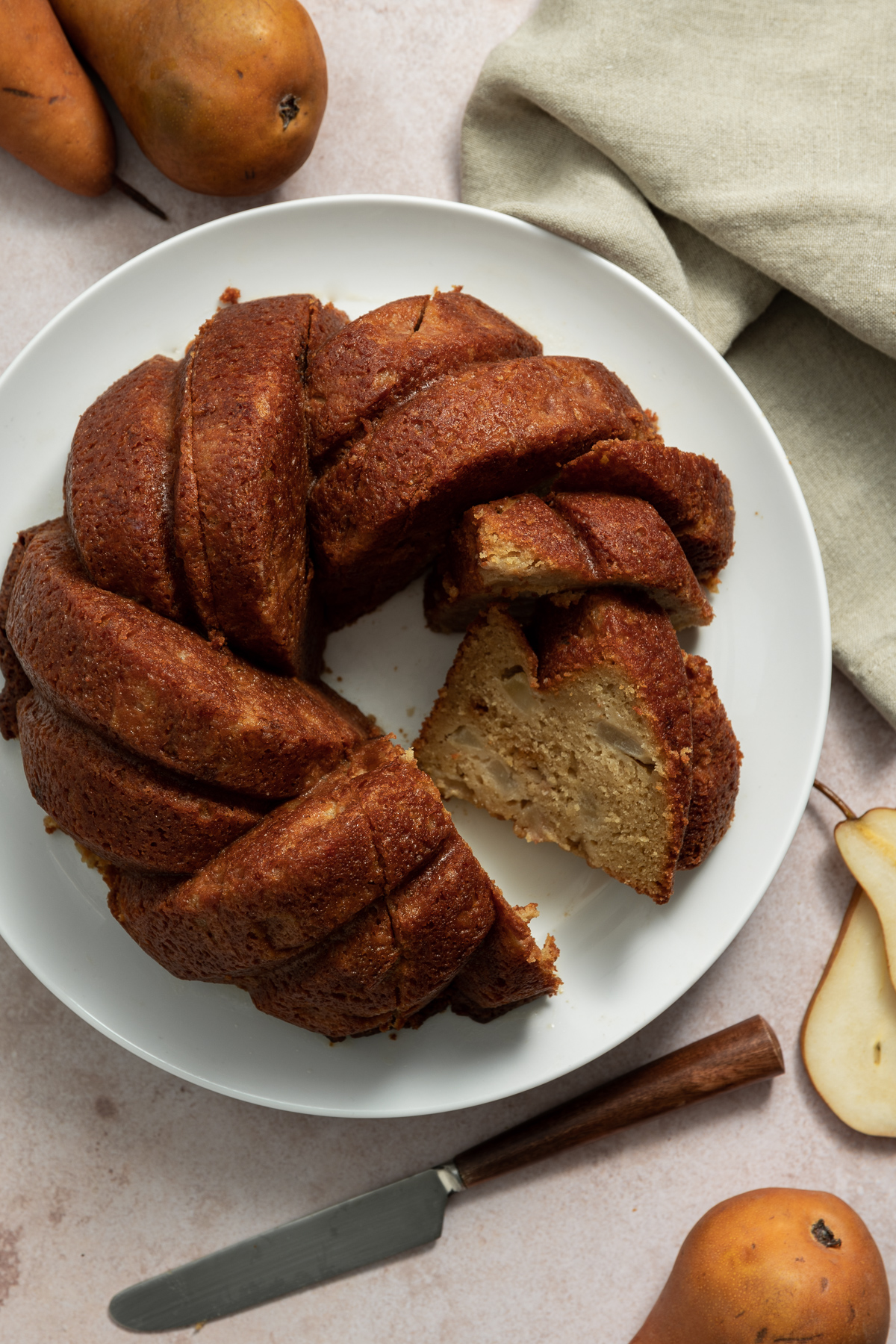 maple pear bundt cake on white plate with whole and sliced bosc pears