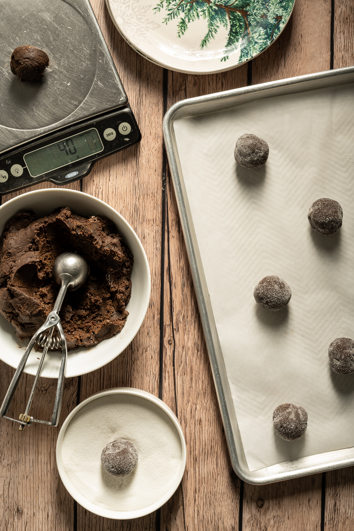 chocolate cookie dough balls being weighed and rolled in sugar some placed on a baking sheet
