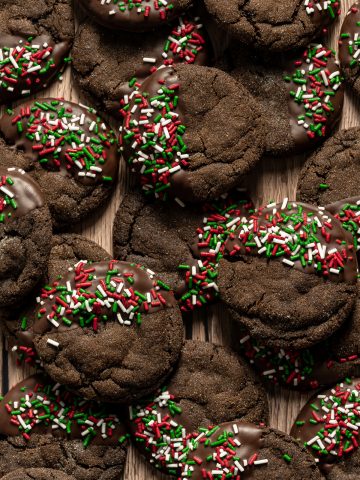 Round chocolate cookies half dipped in chocolate decorated with red white and green sprinkles