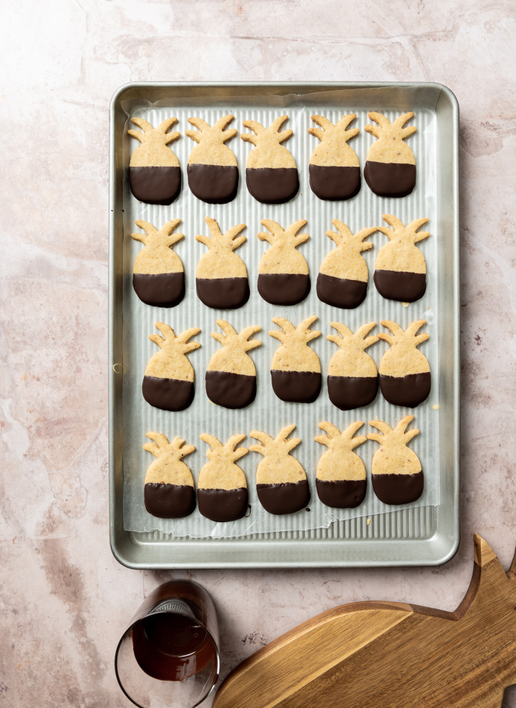 pineapple shaped cookies half dipped in dark chocolate on a baking sheet
