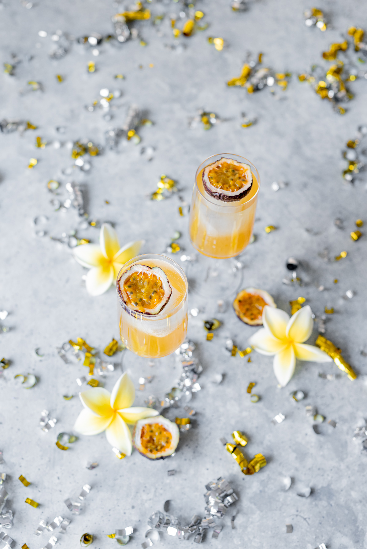 Sweet and sour passionfruit rum fizz cocktail orange liquid in two glasses with passionfruit halves