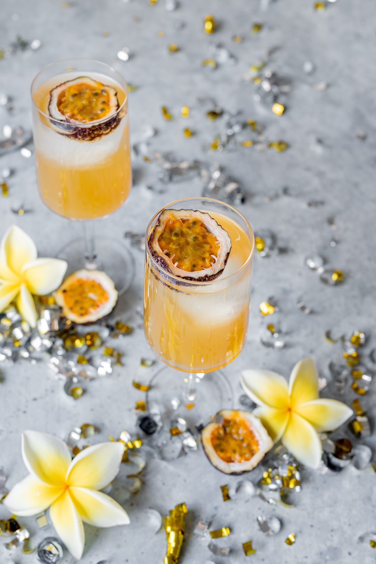 Sweet and sour passionfruit rum fizz cocktail orange liquid in two glasses with passionfruit halves
