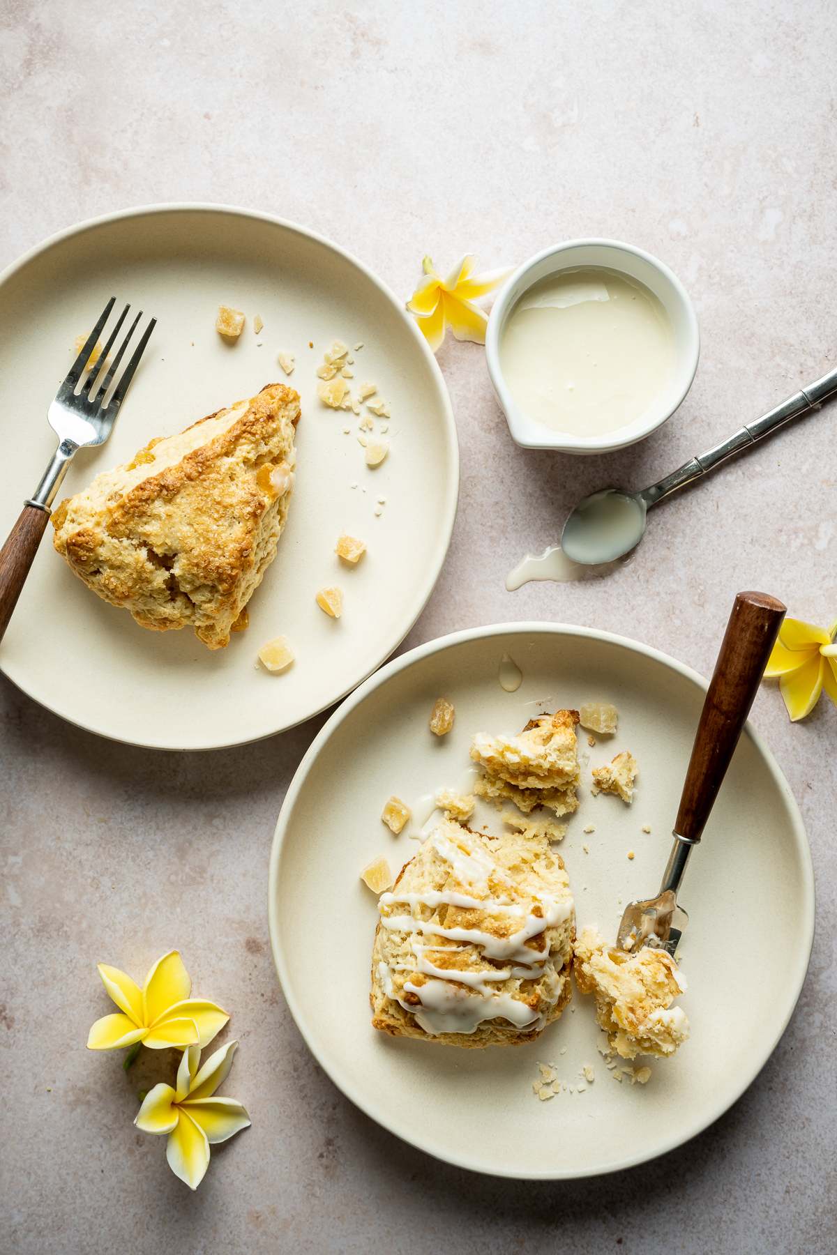 Cut pineapple scone wedges on beige plates with forks bowl of glaze spoon yellow plumerias