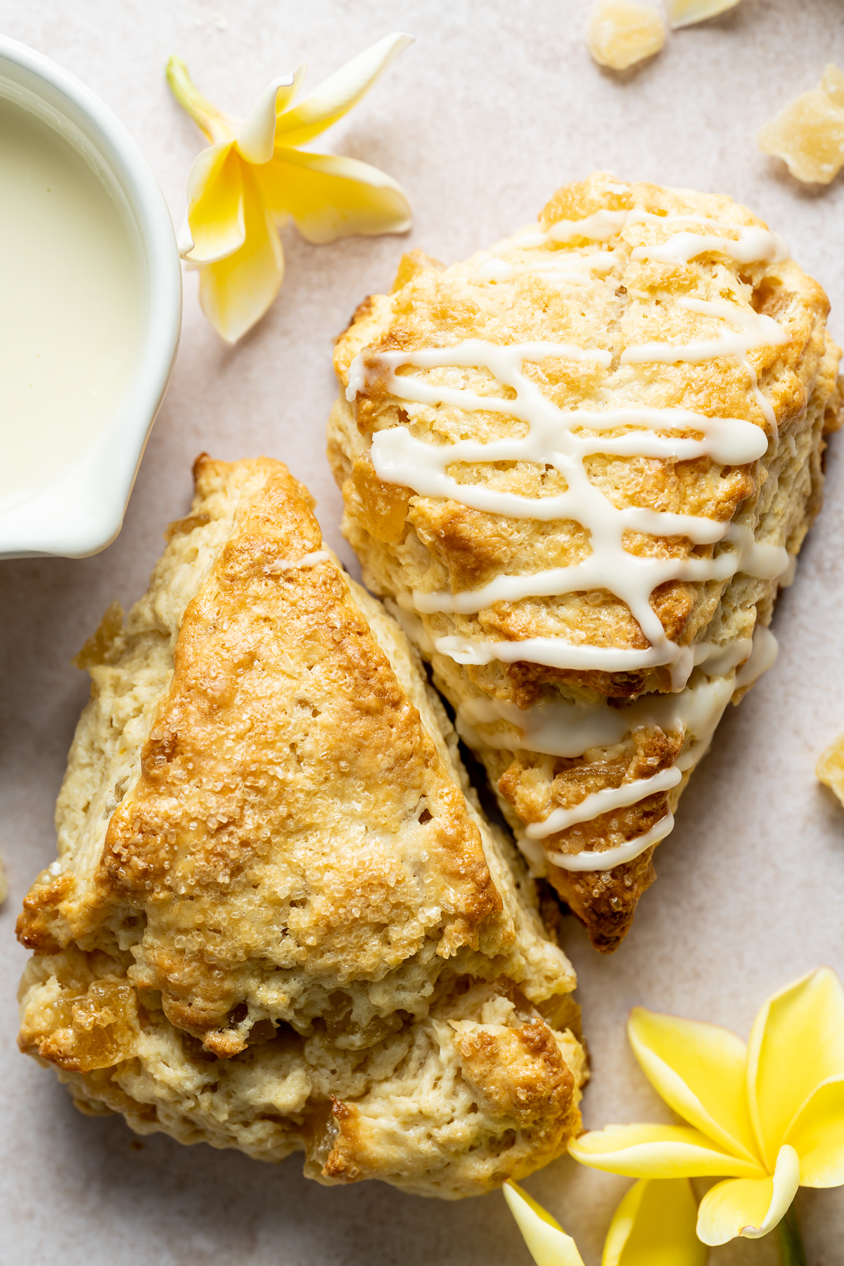 two baked scone wedges one with a white icing drizzle one without yellow plumeria flowers