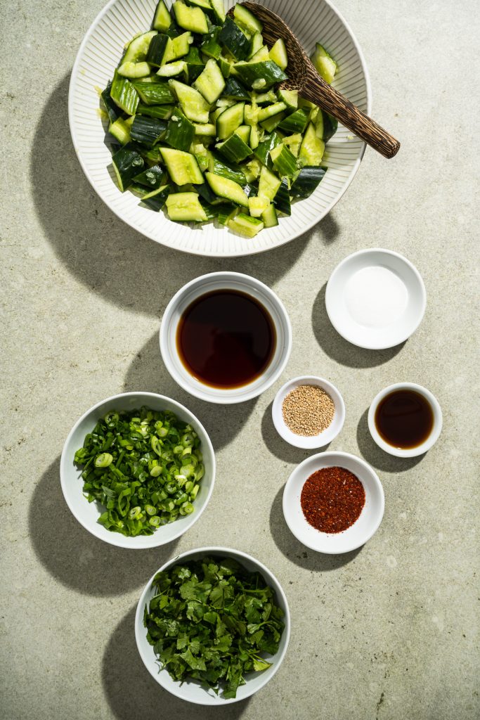 large bowl of cucumber pieces smaller bowls with sauces cilantro and scallions