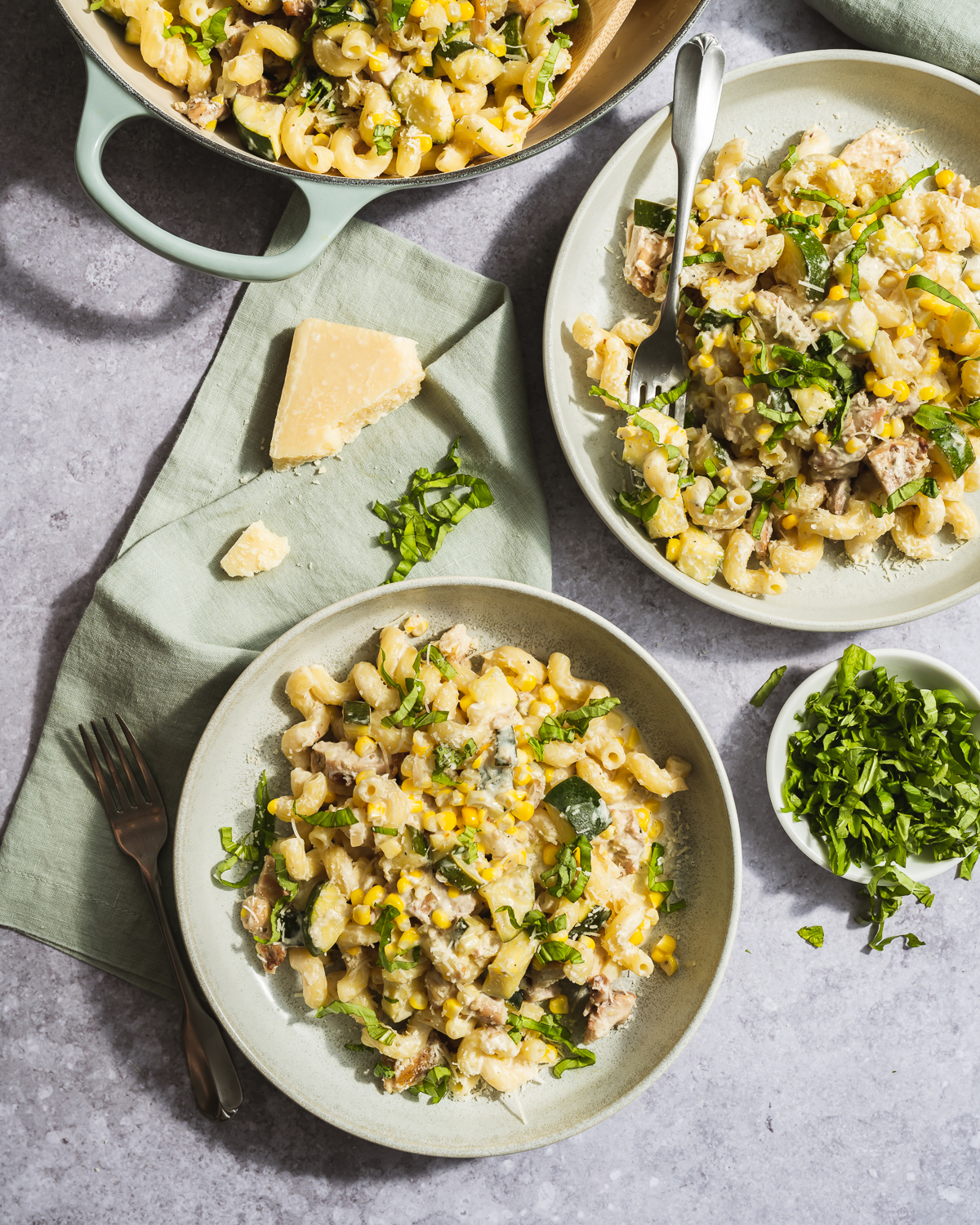 zucchini and corn pasta with basil on plates and a pot green napkin chunk of parmesan cheese two forks