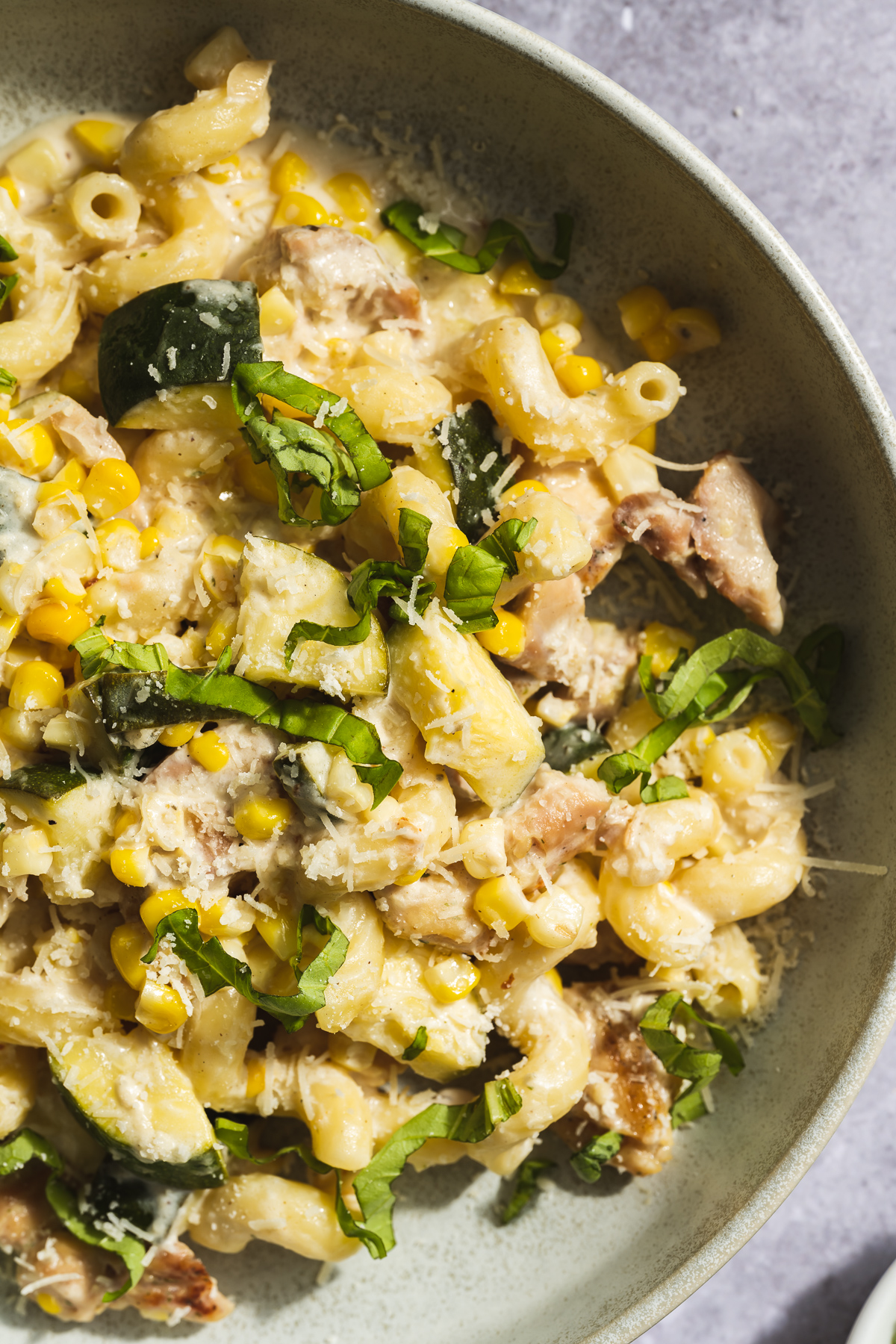 zucchini and corn pasta in a beige plate with basil and parmesan