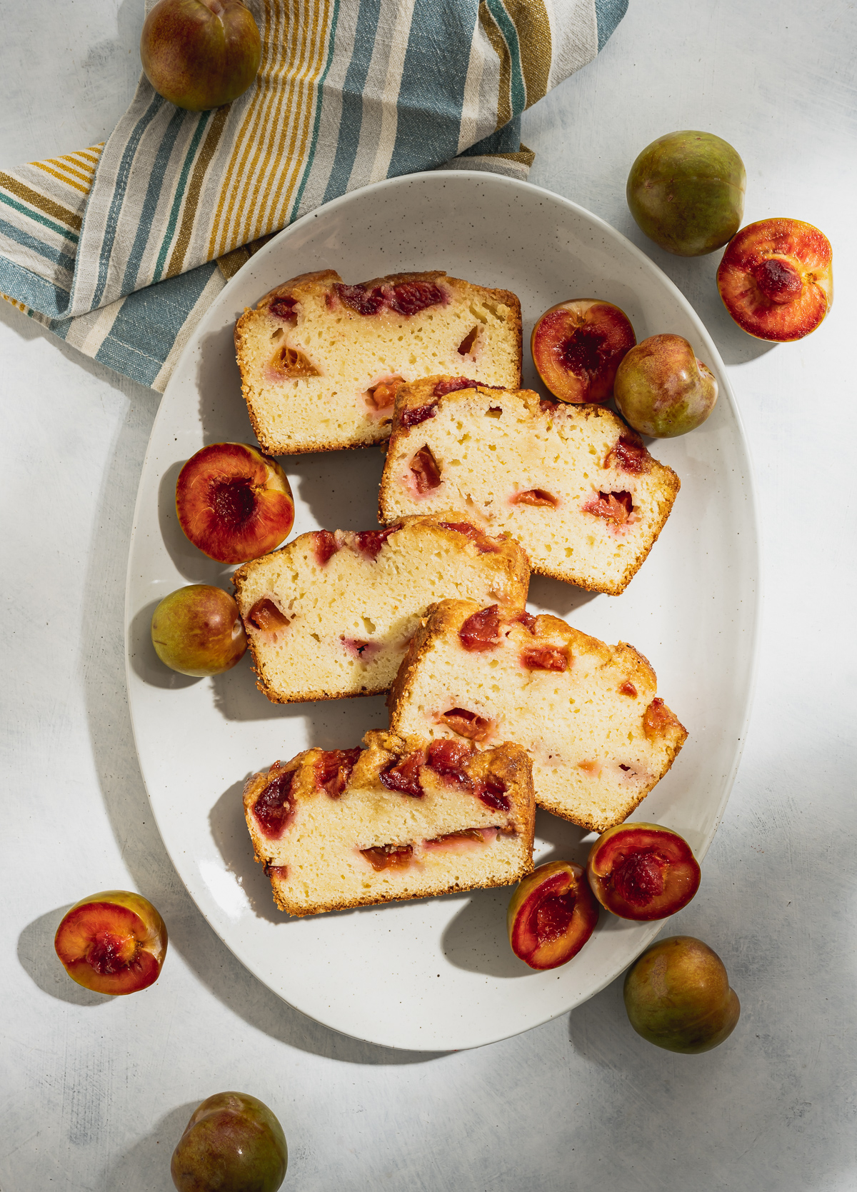 slices of plum pound cake on a light gray speckled platter whole and halved plums