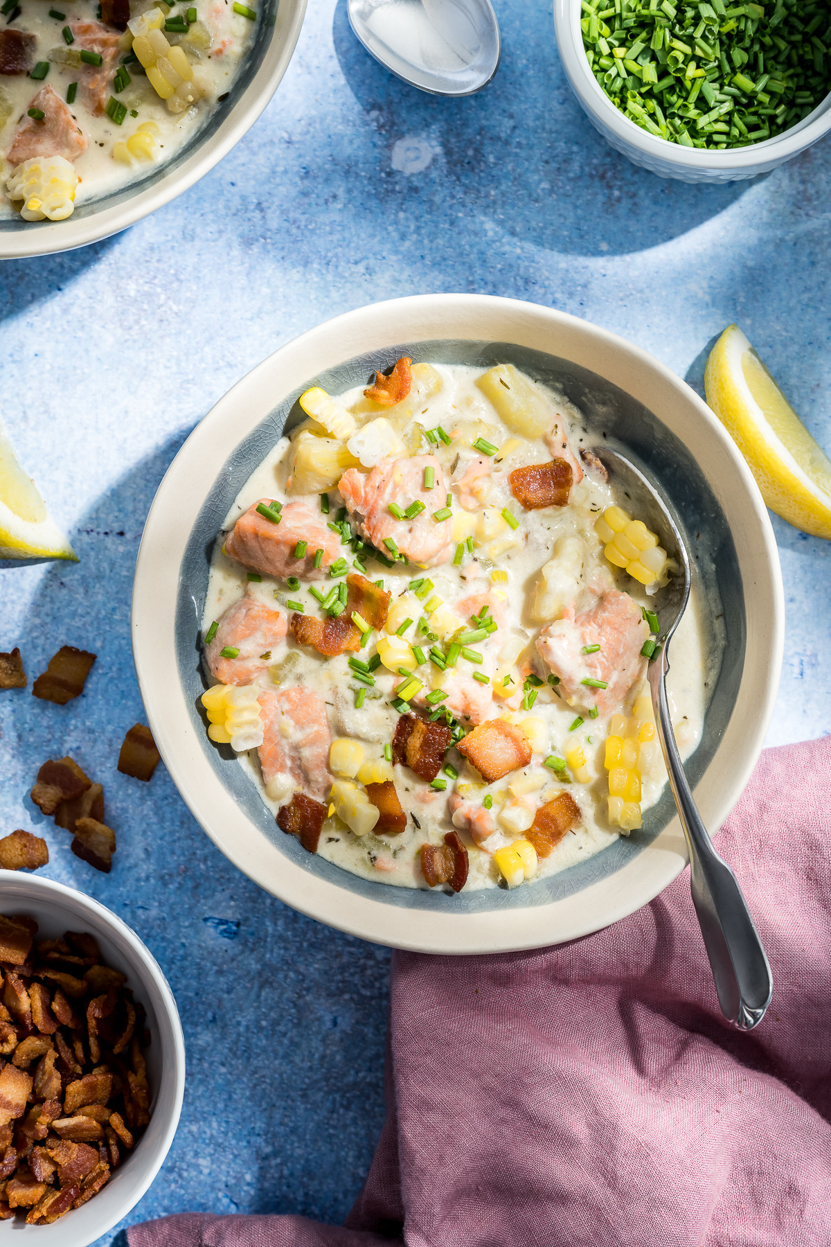 bowl of soup with salmon corn bacon chives lemon slices pink napkin spoon bowl of bacon bits