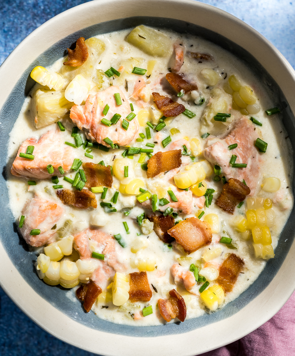 bowl of white chowder with pieces of salmon, corn, bacon and chives