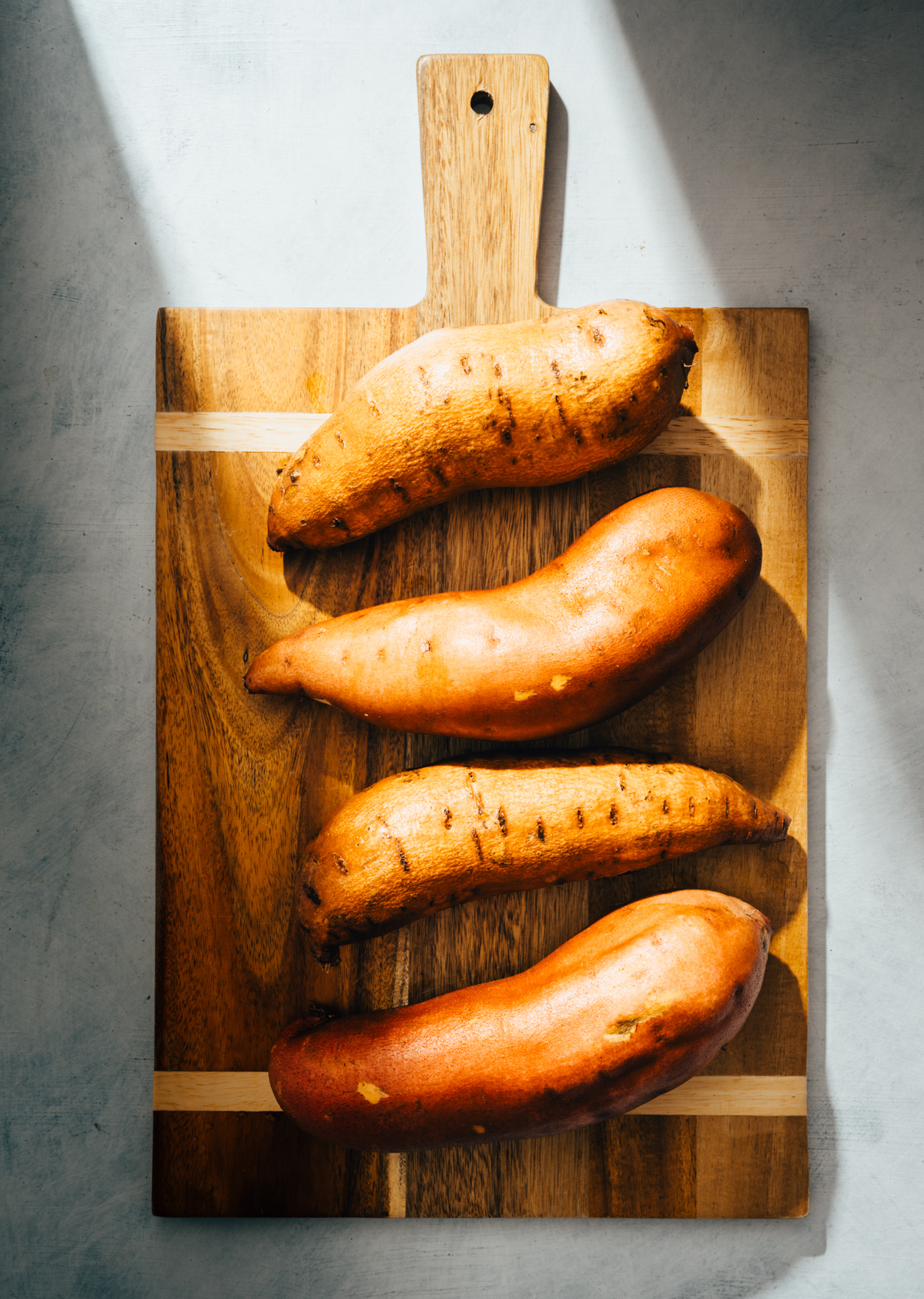 4 whole sweet potatoes on a wood cutting board