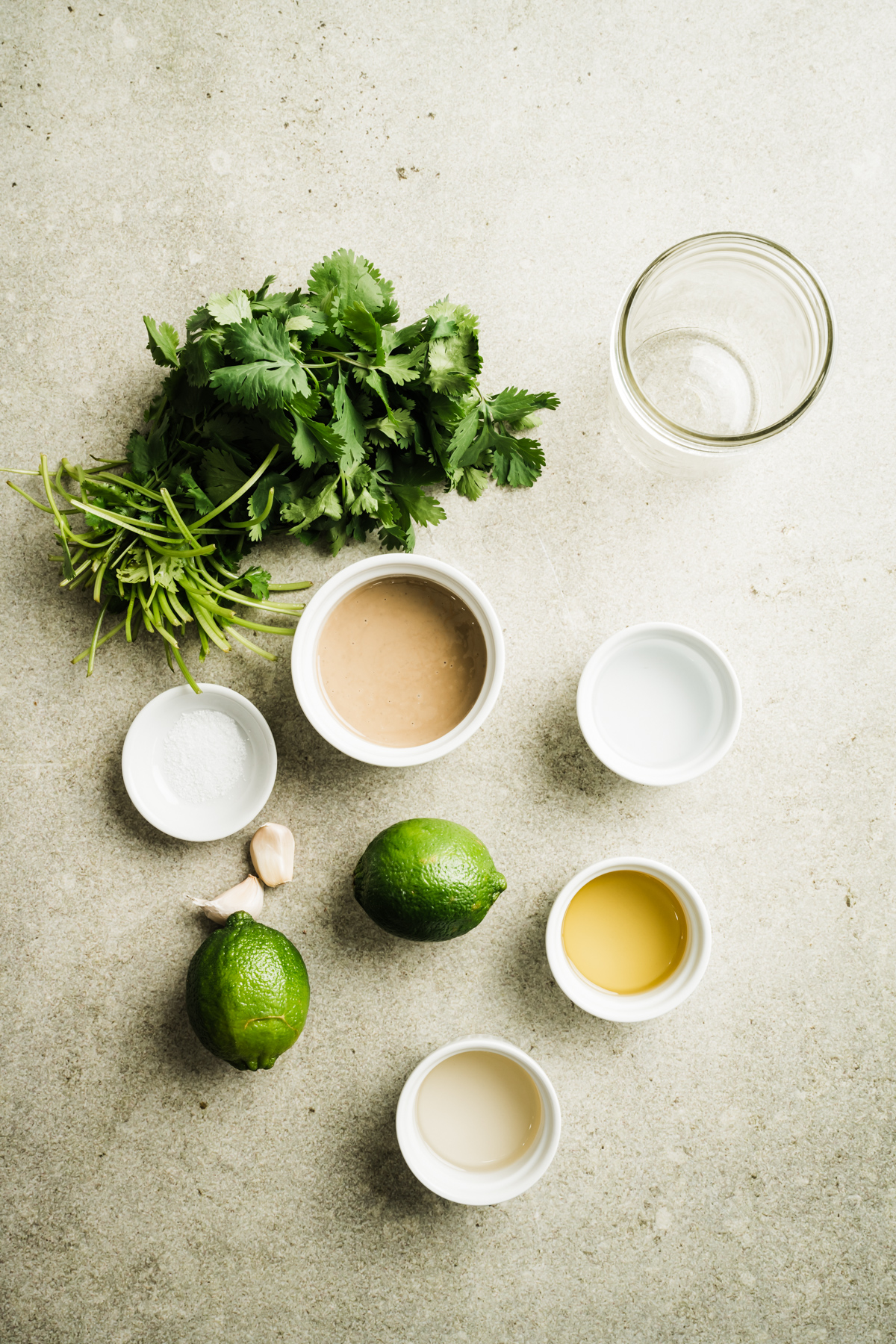 tahini dressing ingredients in varying bowls limes bunch of cilantro empty mason jar