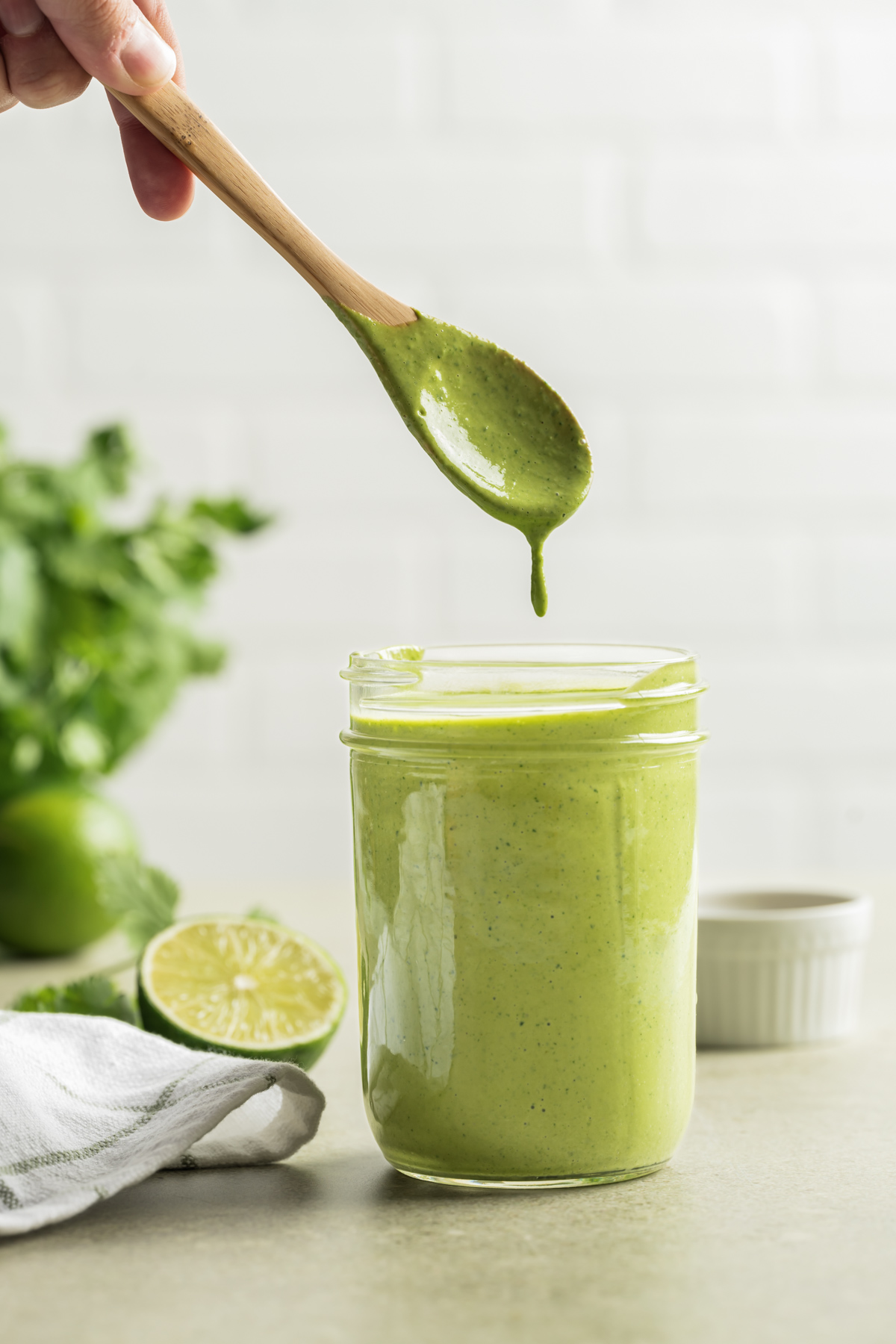 green tahini dressing in a mason jar with a wooden spoon over the jar with dressing dripping back into jar