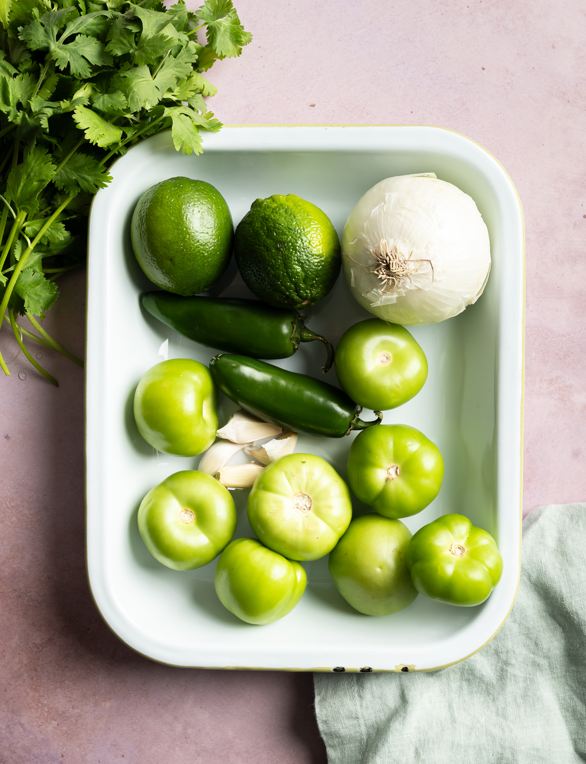 tray with whole tomatillos white onion garlic cloves jalapeños limes cilantro green napkin