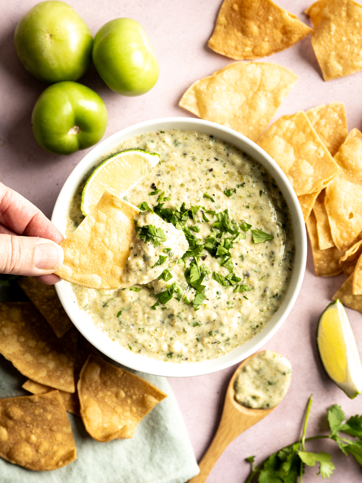 bowl of green salsa with cilantro limes chips wooden spoon green napkin chip being dipped into salsa