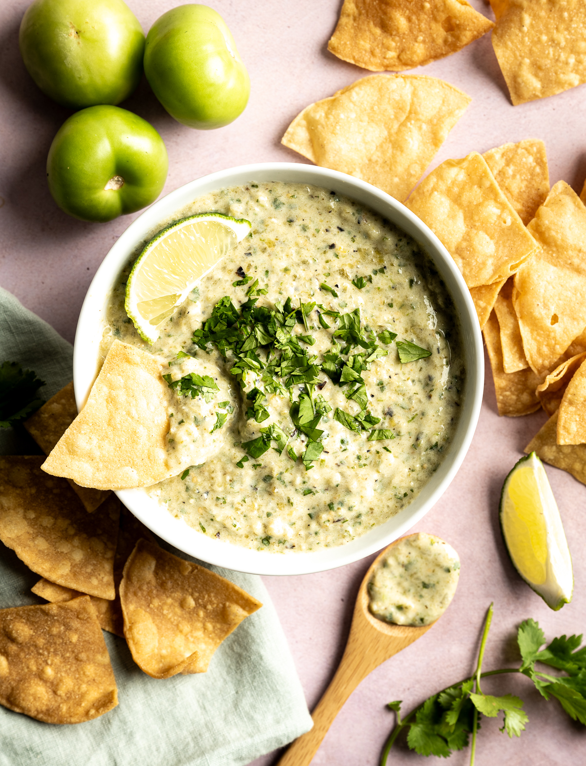 bowl of green salsa with cilantro limes chips wooden spoon green napkin