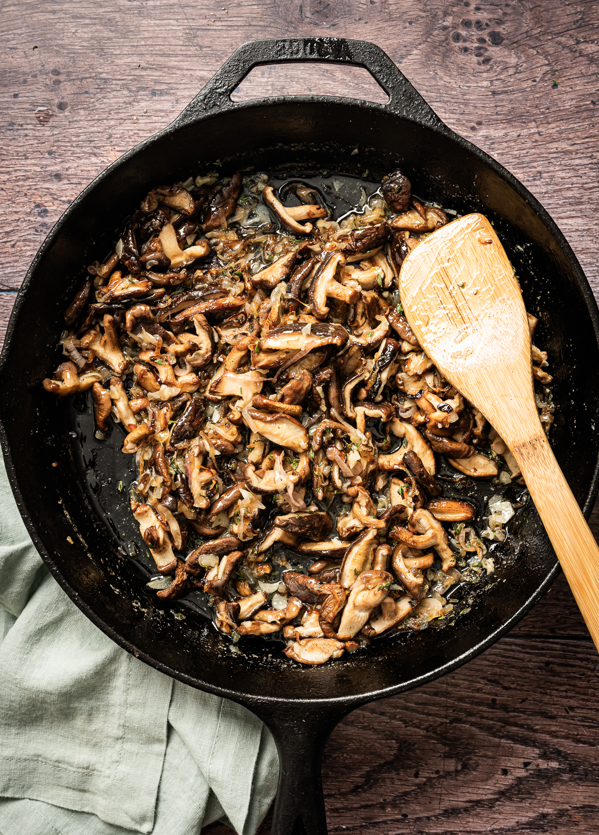 satueed shiitake mushrooms caramelized shallots chopped fresh thyme with sliced garlic and melted butter in cast iron pan bamboo spatula
