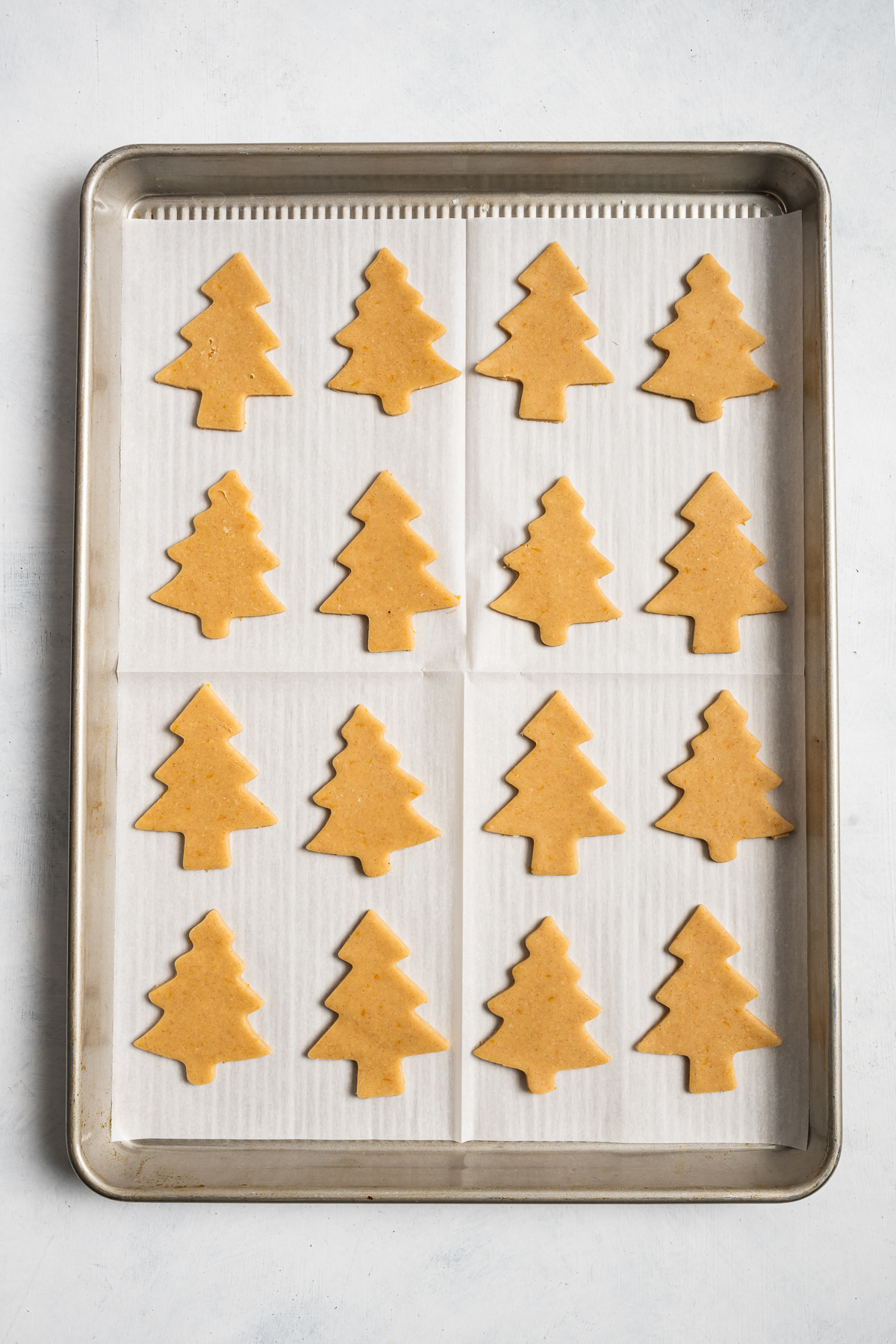 tree shaped cookies on parchment paper lines baking sheet