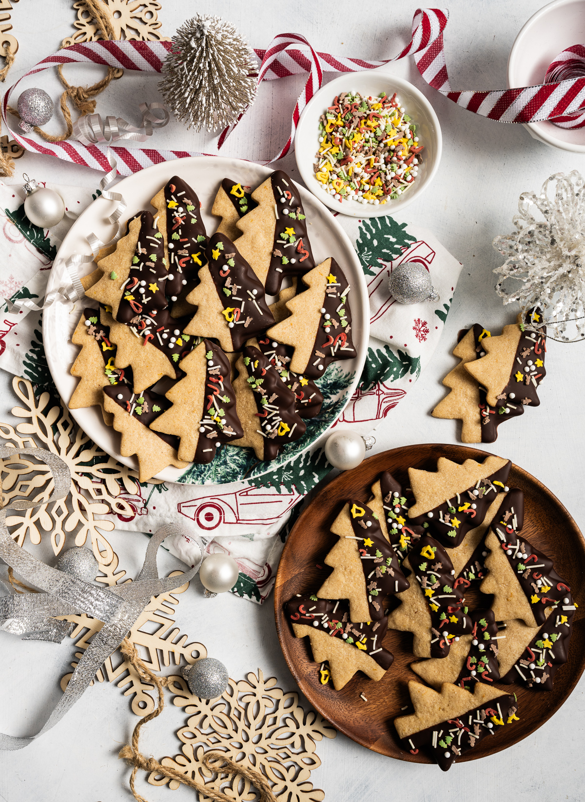 tree shaped cookies half dipped in chocolate with sprinkles bowl of sprinkles ornaments red and white striped ribbon