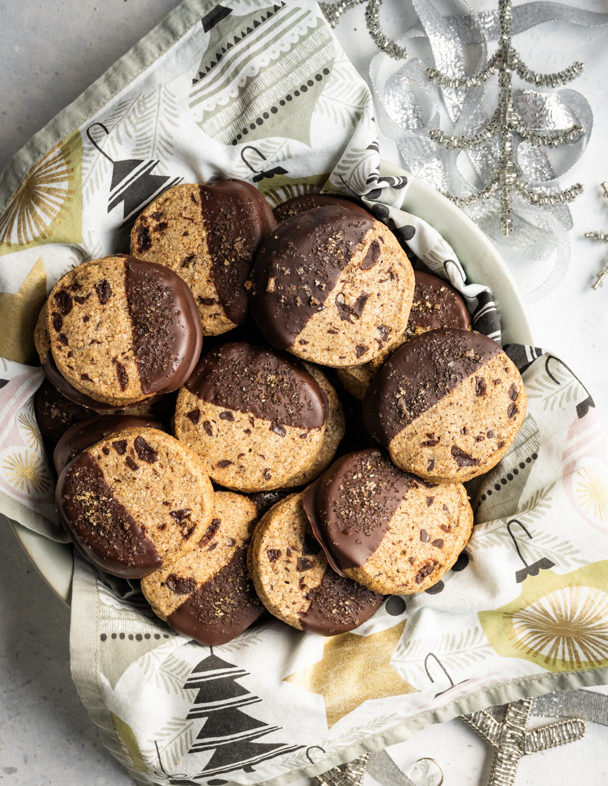 half chocolate dipped espresso shortbread cookies in a bowl with christmas ornament napkin silver snowflakes silver ribbon
