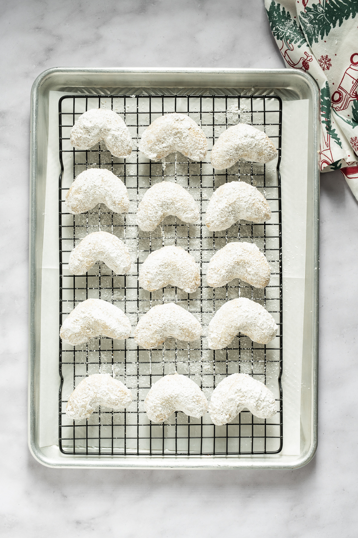 white confectioners sugar coated almond crescent cookies on a wire cooling rack