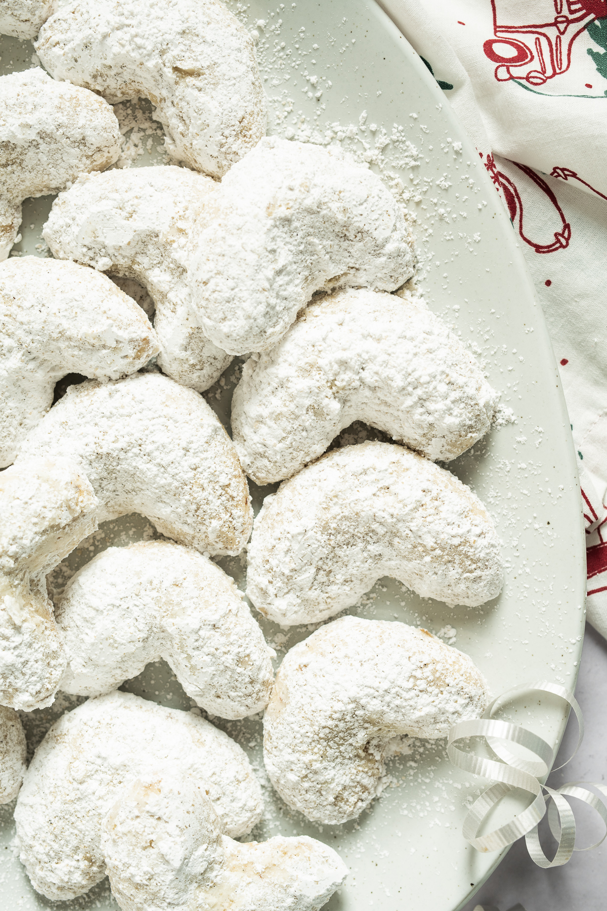 white confectioners sugar coated almond crescent cookies on a white plate