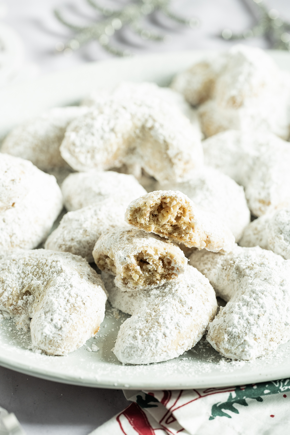 white confectioners sugar coated almond crescent cookies on a white plate