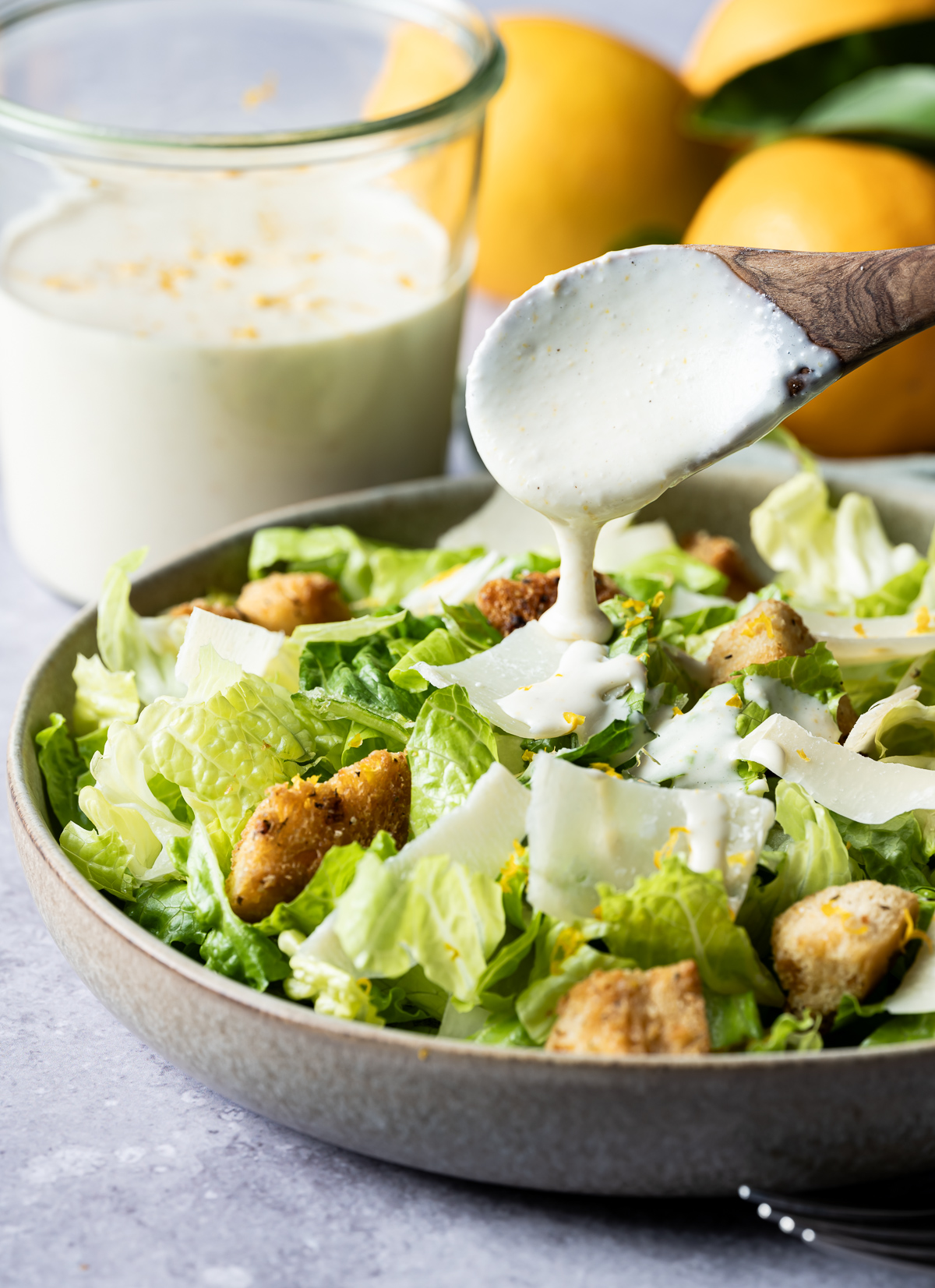 meyer lemon Caesar dressing being spooned over a bowl of lettuce with croutons whole Meyer lemons dressing in a jar
