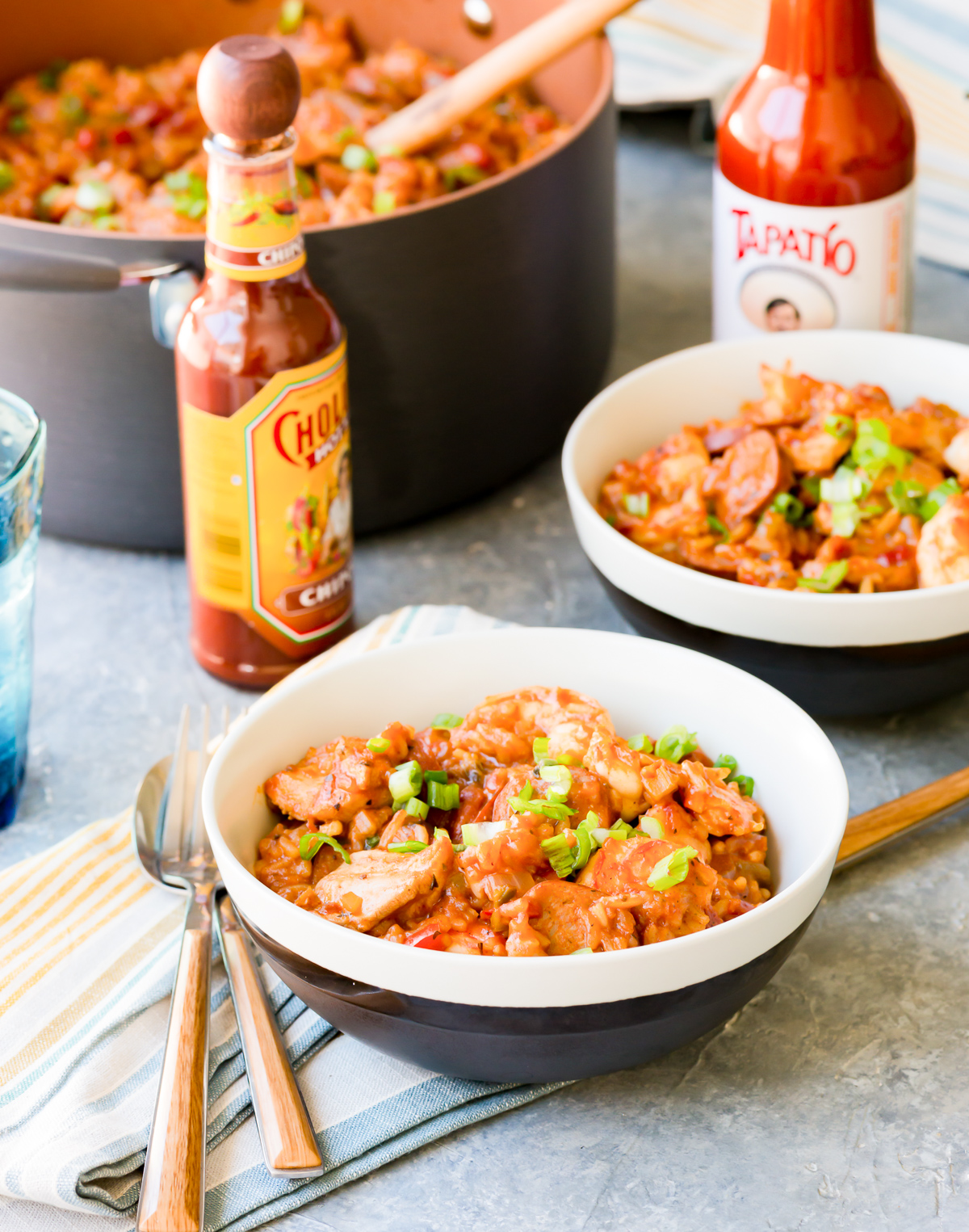 bowls of jambalaya with striped napkins forks and spoons bottle of tapatio bottle of cholula