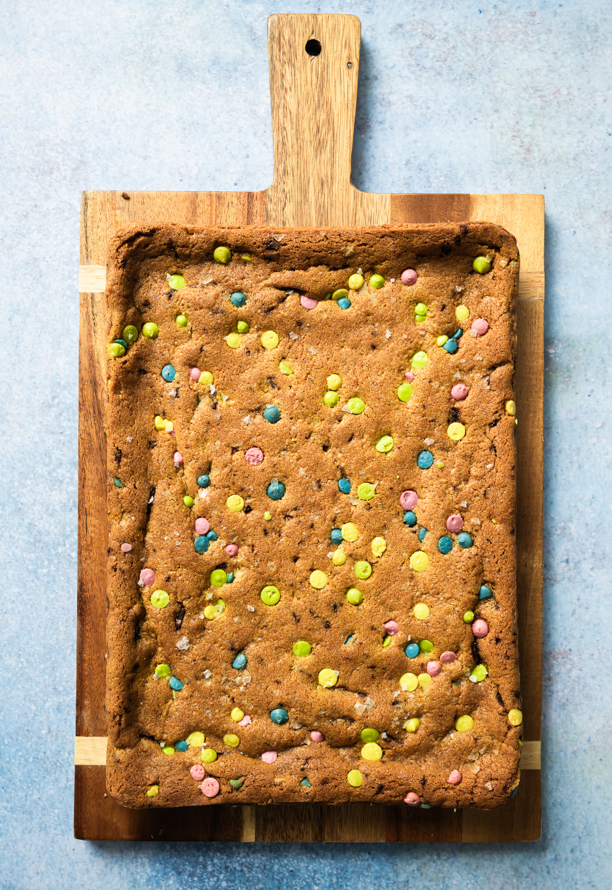 slab of uncut cookie bars with rainbow chips on cutting board