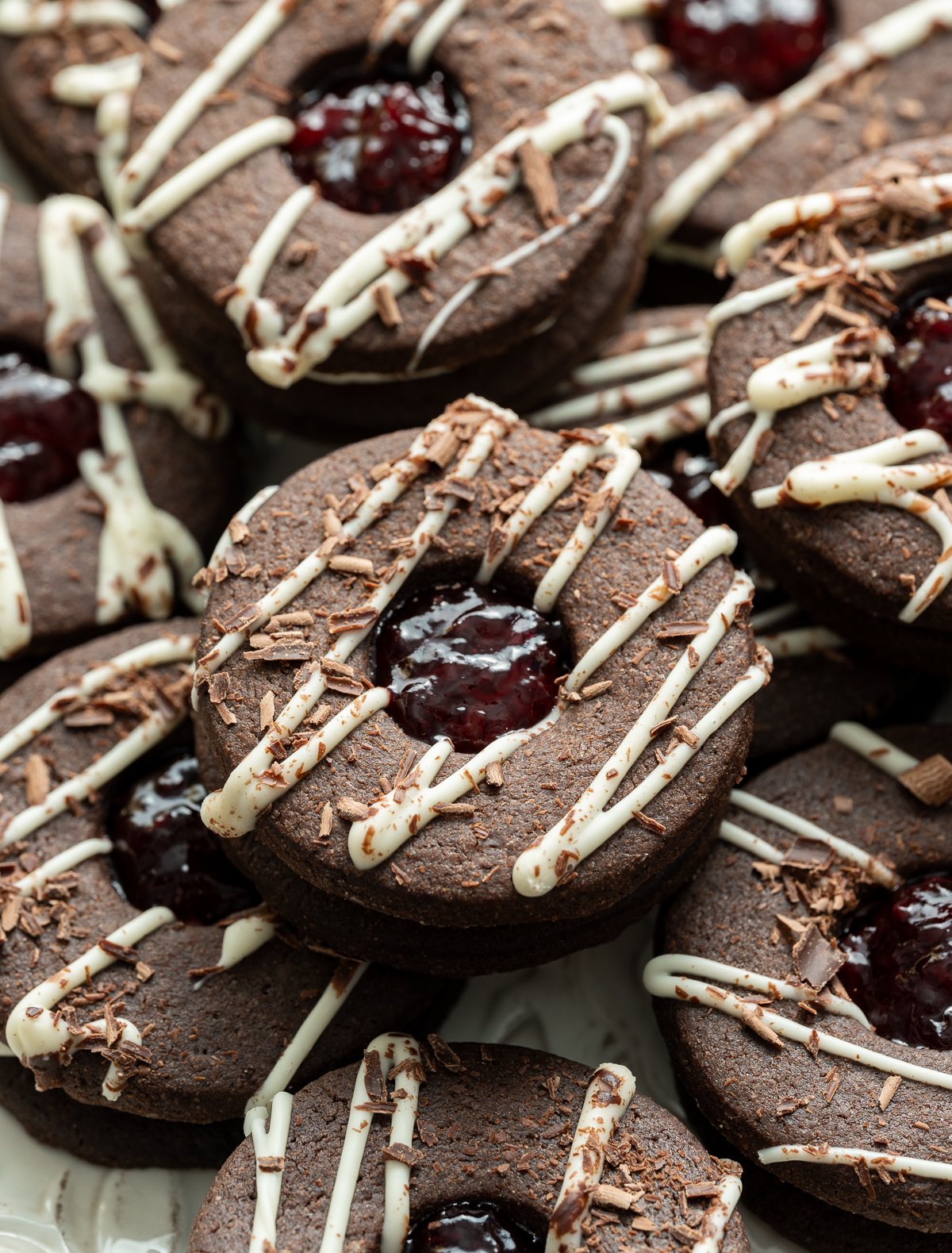 black forest linzer cookies chocolate cookies with white chocolate ganache and sour cherry jam filling white chocolate drizzle chocolate shavings