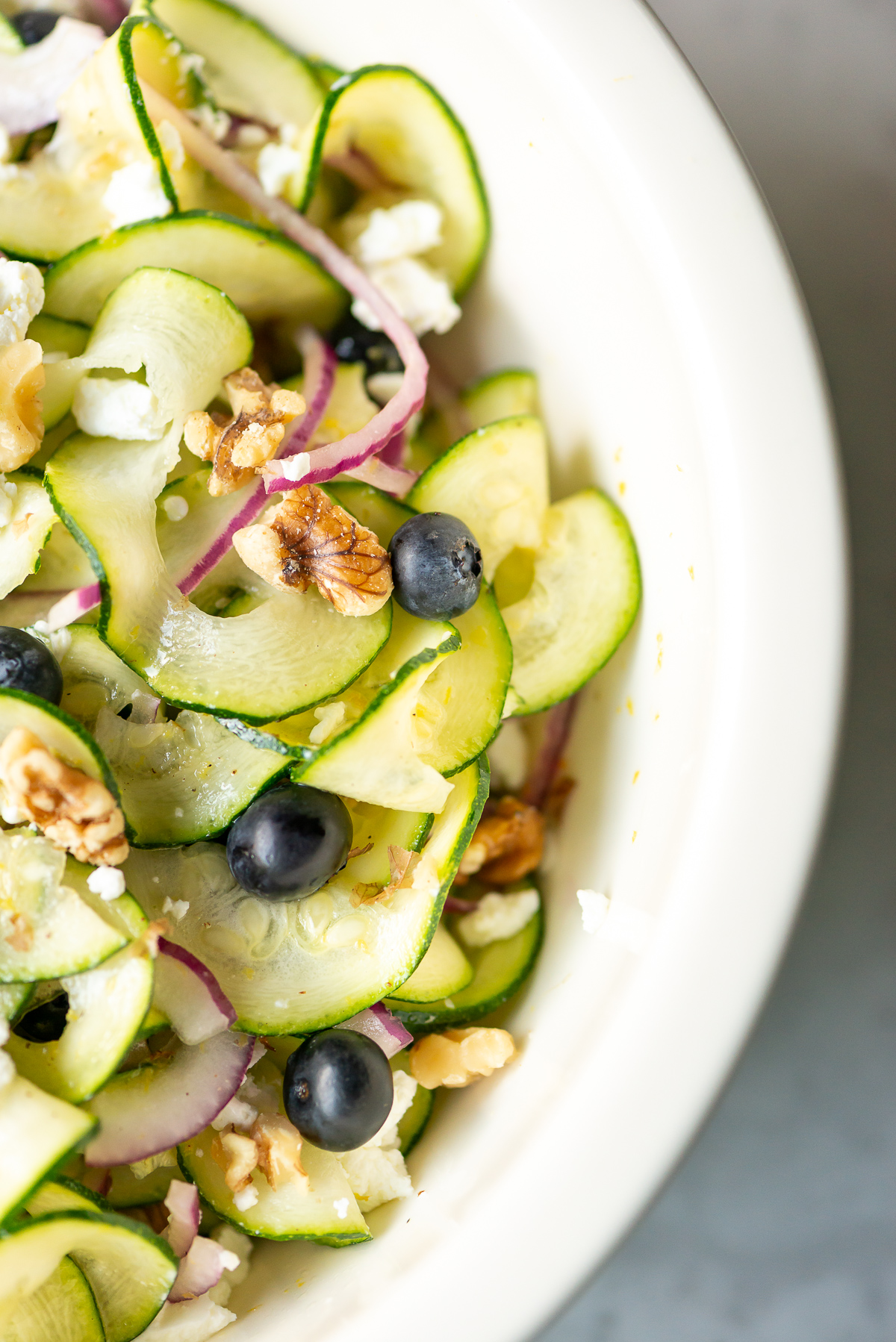 bowl full of zucchini ribbon salad with red onion slices blueberries walnut pieces and goat cheese crumbles