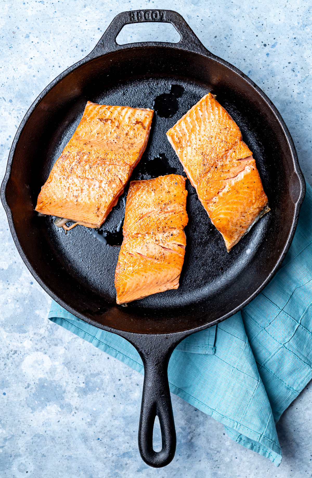 three sockeye salmon fillet segments cooking in a cast iron pan
